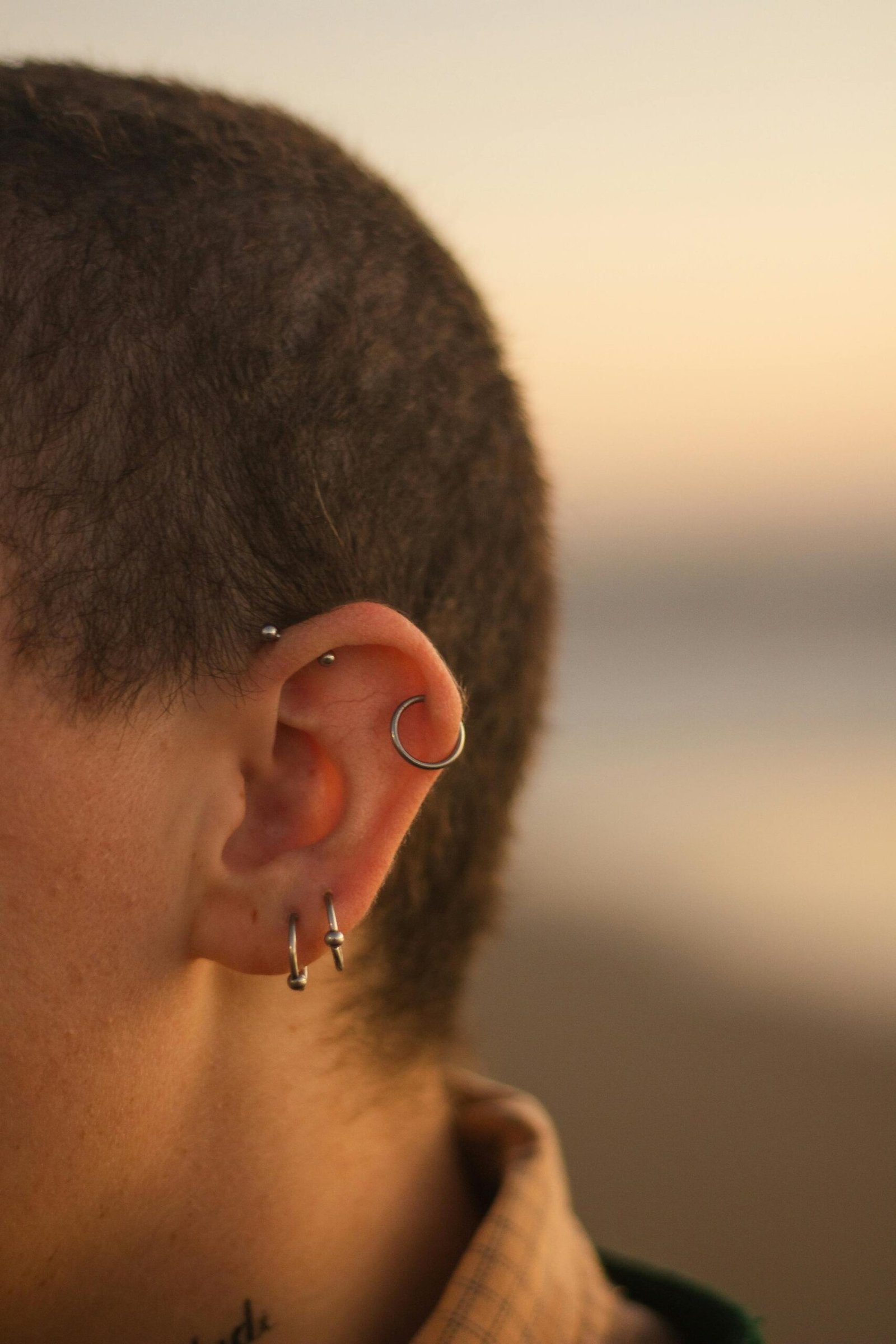 A close-up image of an ear with multiple piercings featuring hoop earrings at sunset.